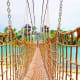 Rope suspension bridge over turquoise water with tropical beach and palm trees at adventure theme park